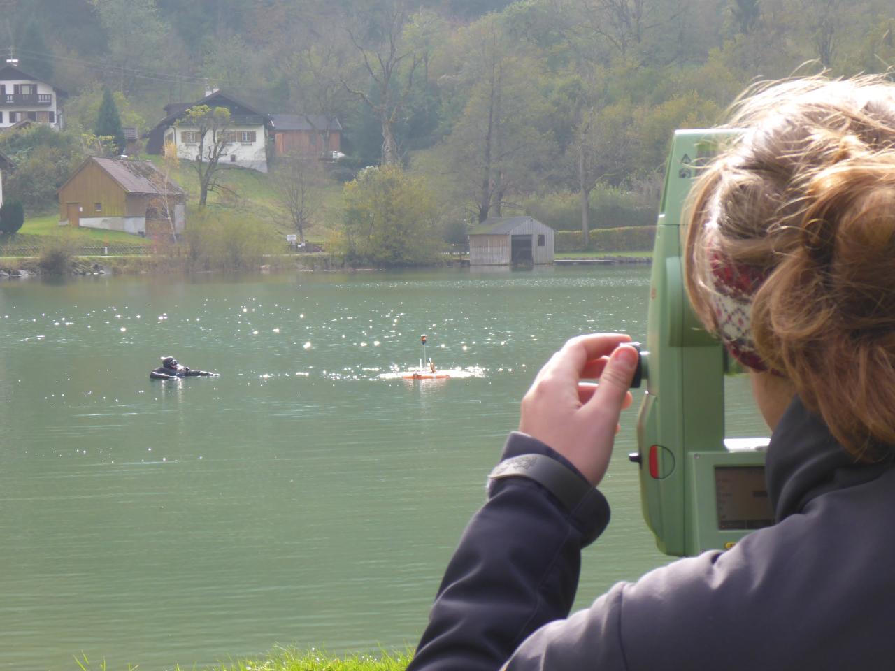 Eine Frau steht am Tachymeter und blickt auf den See, wo ein Taucher an der Oberfläche erkennbar ist