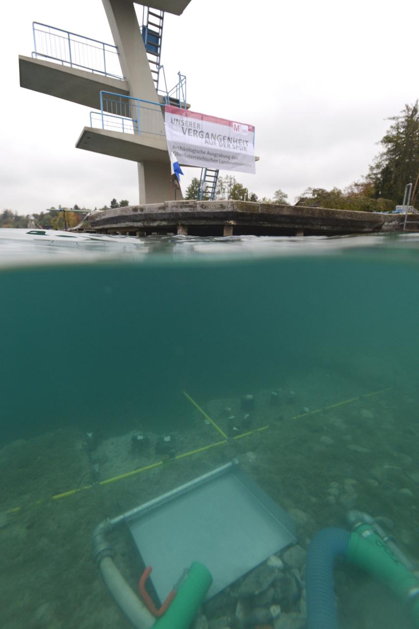 Man sieht den Sprungturm in Seewalchen und zur Hälfte des Bildes unter Wasser eine Kamera über dem Grabungsschnitt