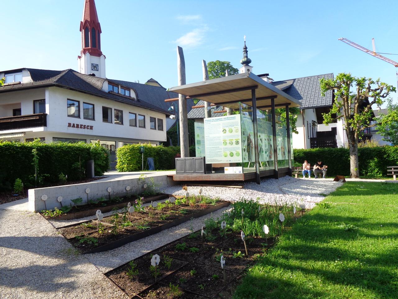 Direkt am Pfahlbaupavillon sind 2 Beete angelegt, im Hintergrund sieht man die Kirche