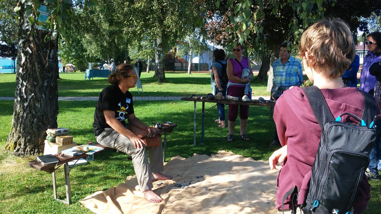 Marco beim flintknapping vor einer Besuchergruppe