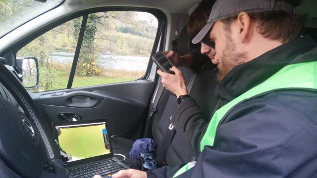 2 Personen sitzen in einem PKW und betrachten einen Laptop