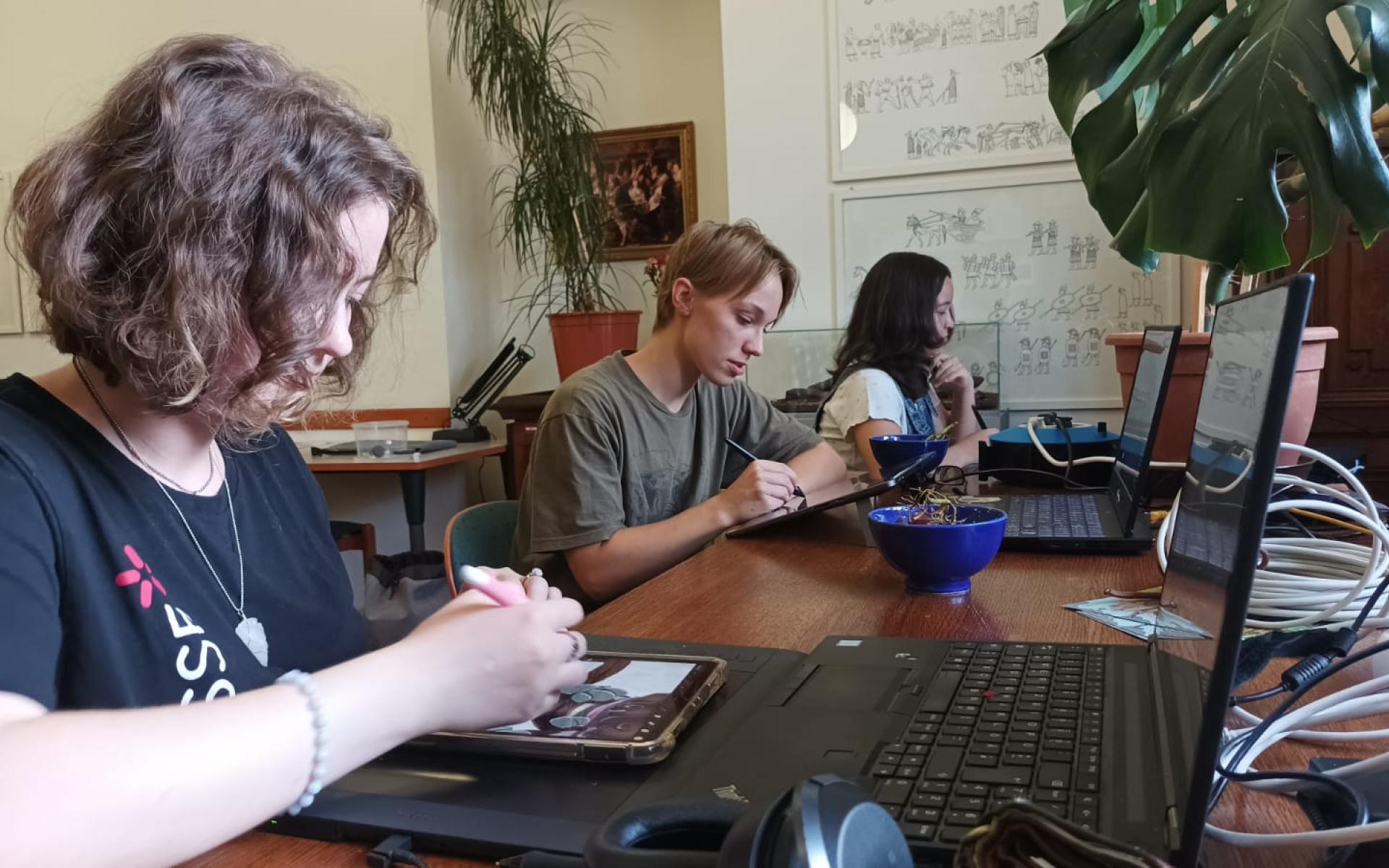 3 Personen sitzen an einem Schreibtisch und arbeiten an ihren Computern