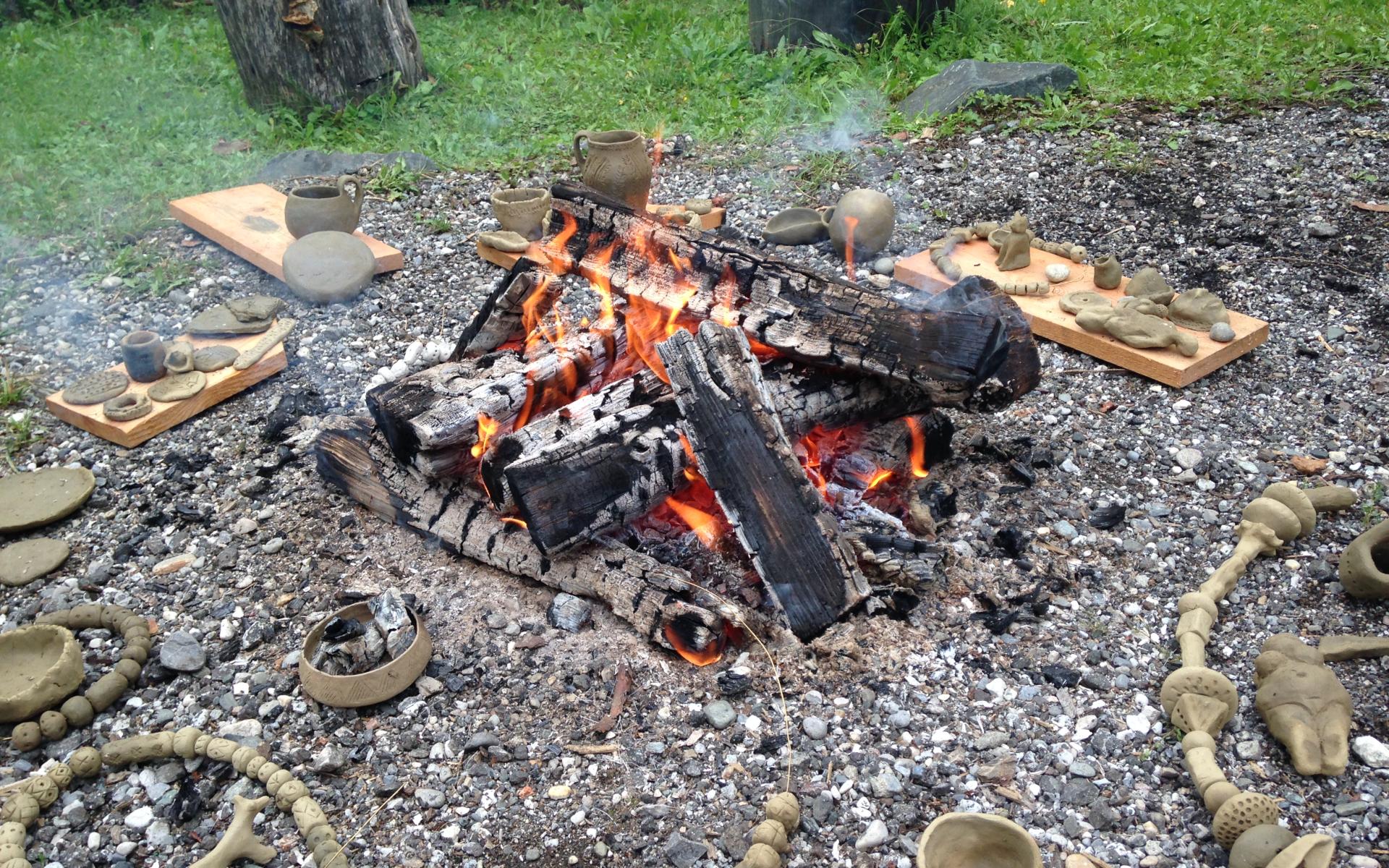 Feuchte Keramikgefäße liegen rund um brennende Holzscheite