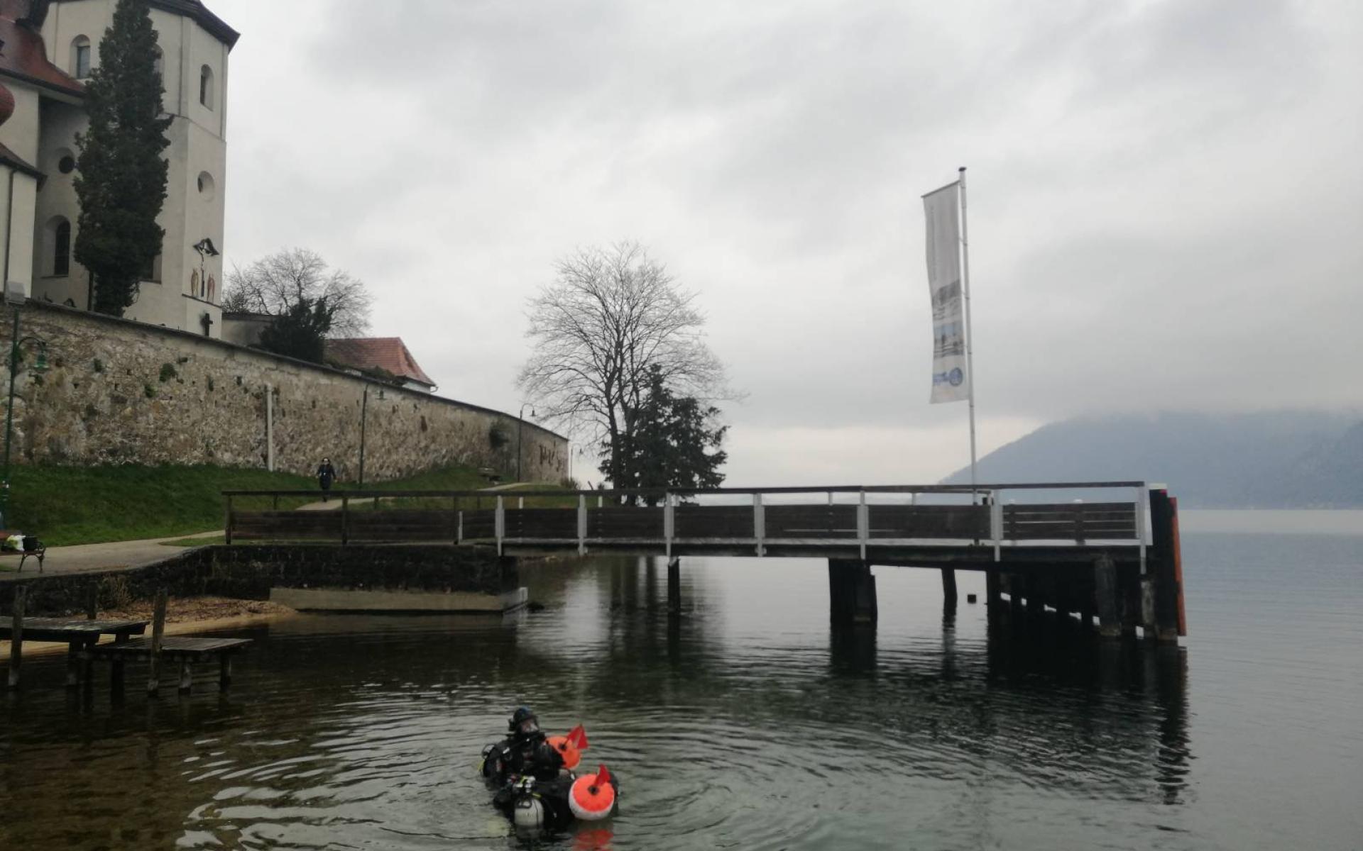 Taucher:Innen im Flachwasserbereich des Traunsees vor dem Hintergrund des Klosters Traunkirchen