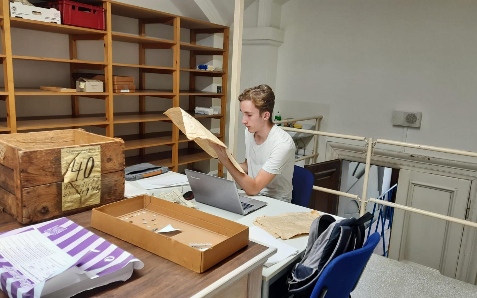 Eine Person sitzt in einem Archiv und liest eine alte Zeitung