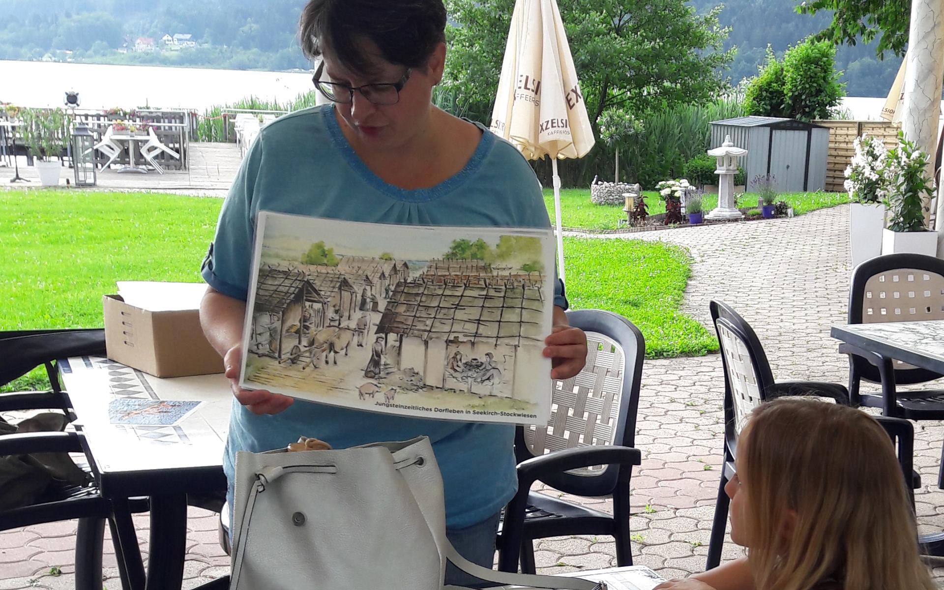 Lieselore erklärt Kindern etwas anhand einer Illustration in einem Strandcafe.