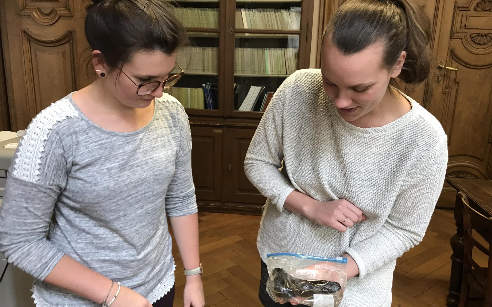 Der Bärenknochen aus dem Keutschacher See wird von 2 Frauen begutachtet.