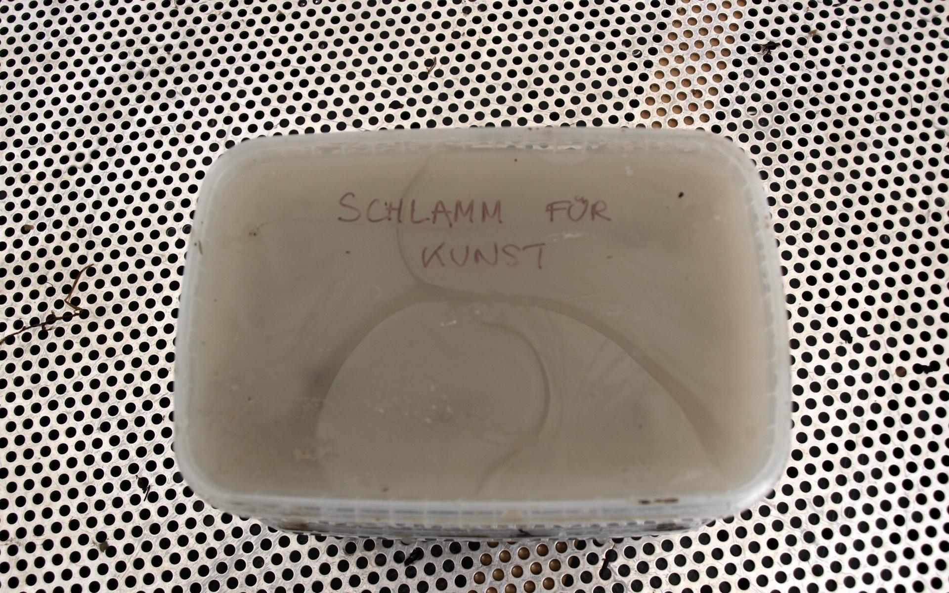 Ein Plastikbecher mit Schlamm und der Aufschrift "Schlamm für Kunst"