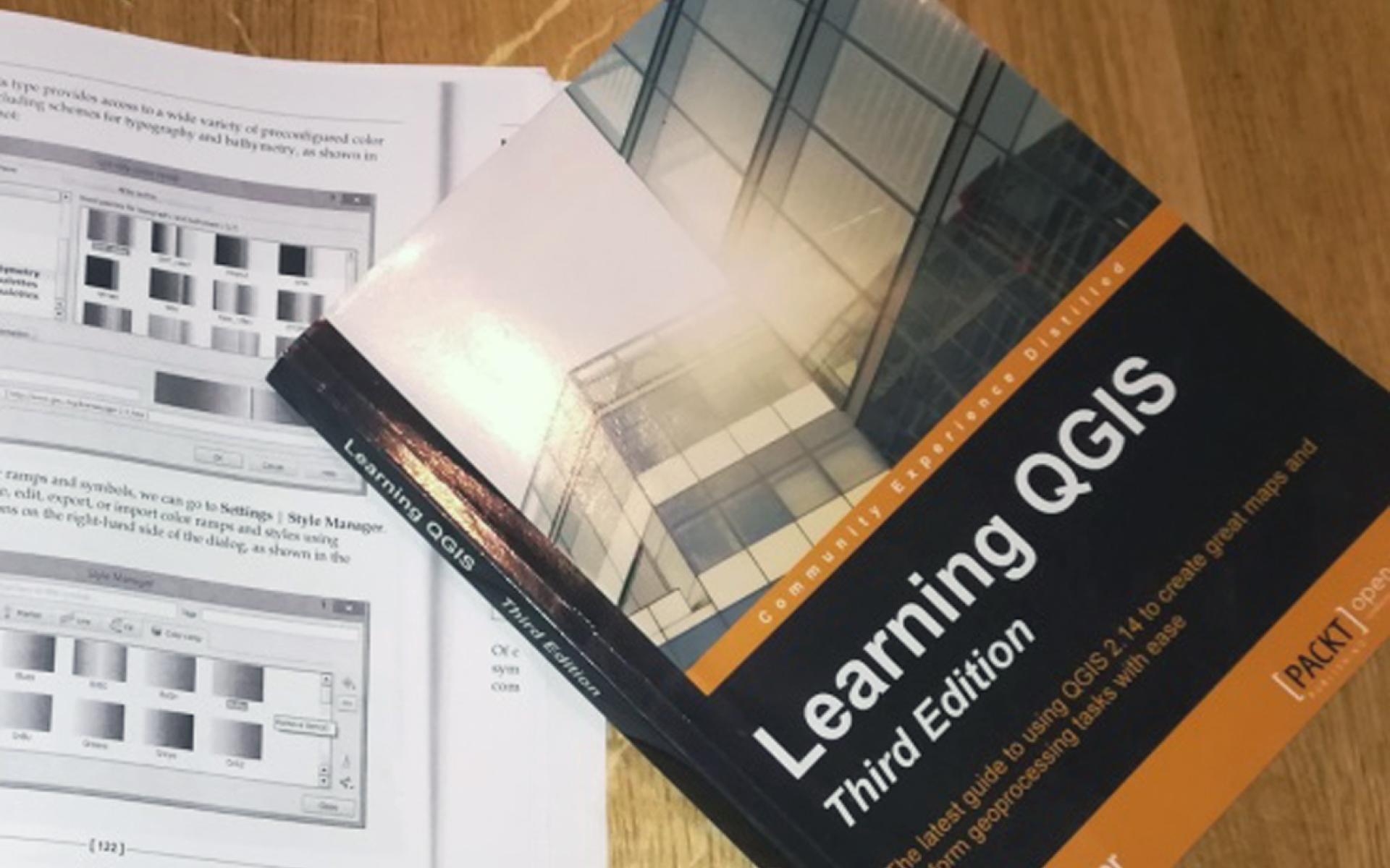Ein Buch "Learning QGIS" auf einem weiteren geöffneten Buch