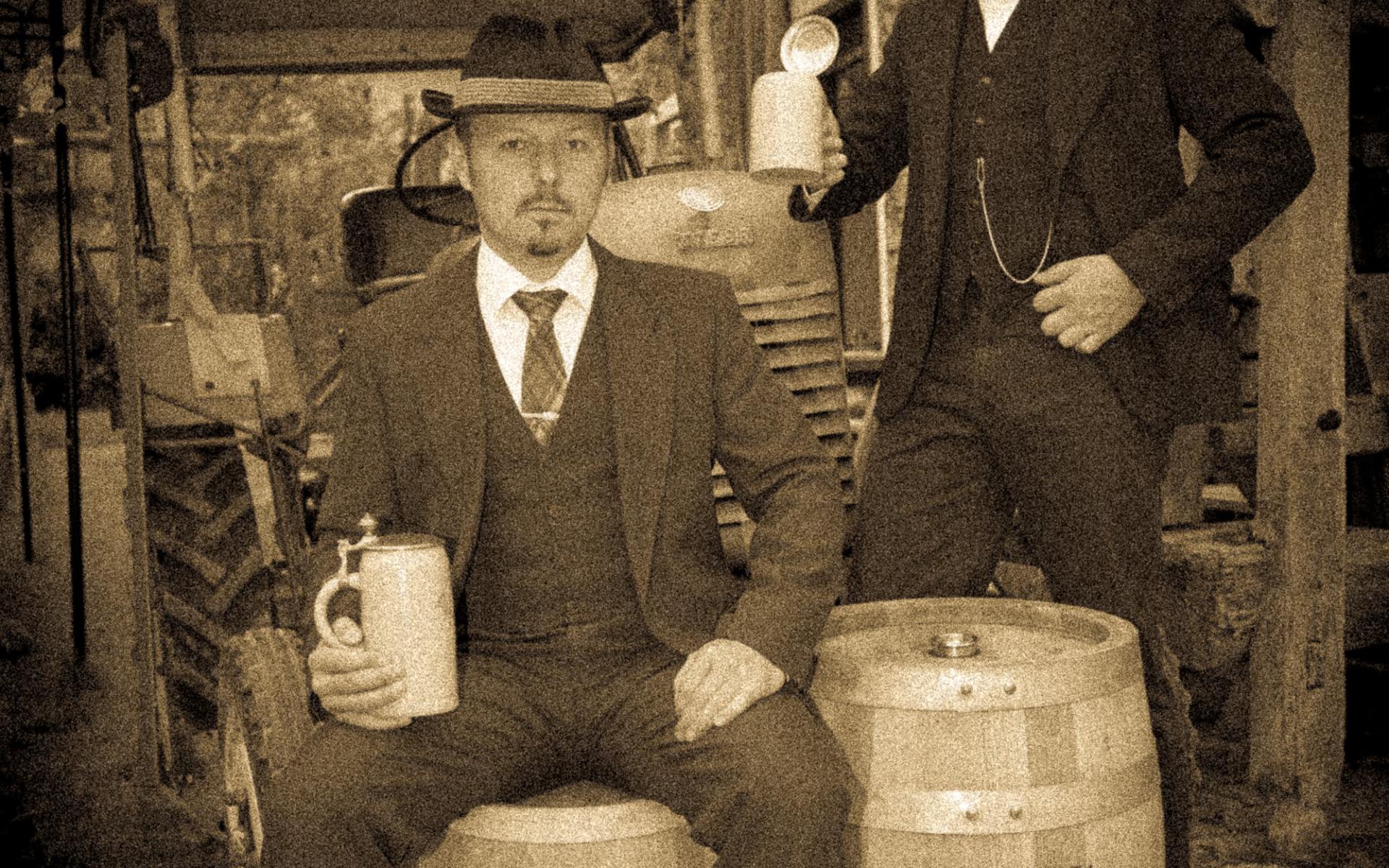Die Brüder Kaltenböck neben Bierfässern und mit Bierkrügen in der Hand