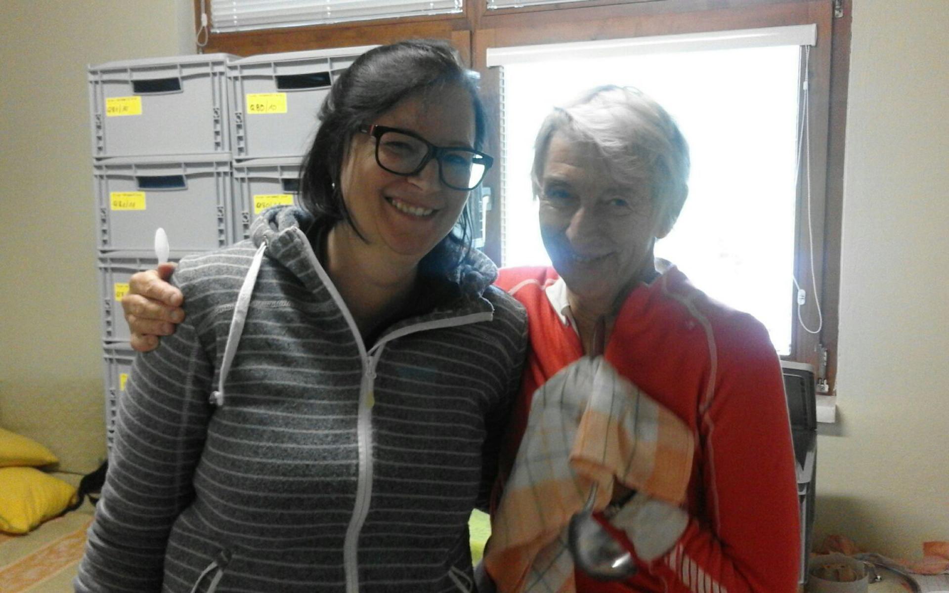 Bärbel und Heike umarmen sich vor einem Fenster und grauen Kisten