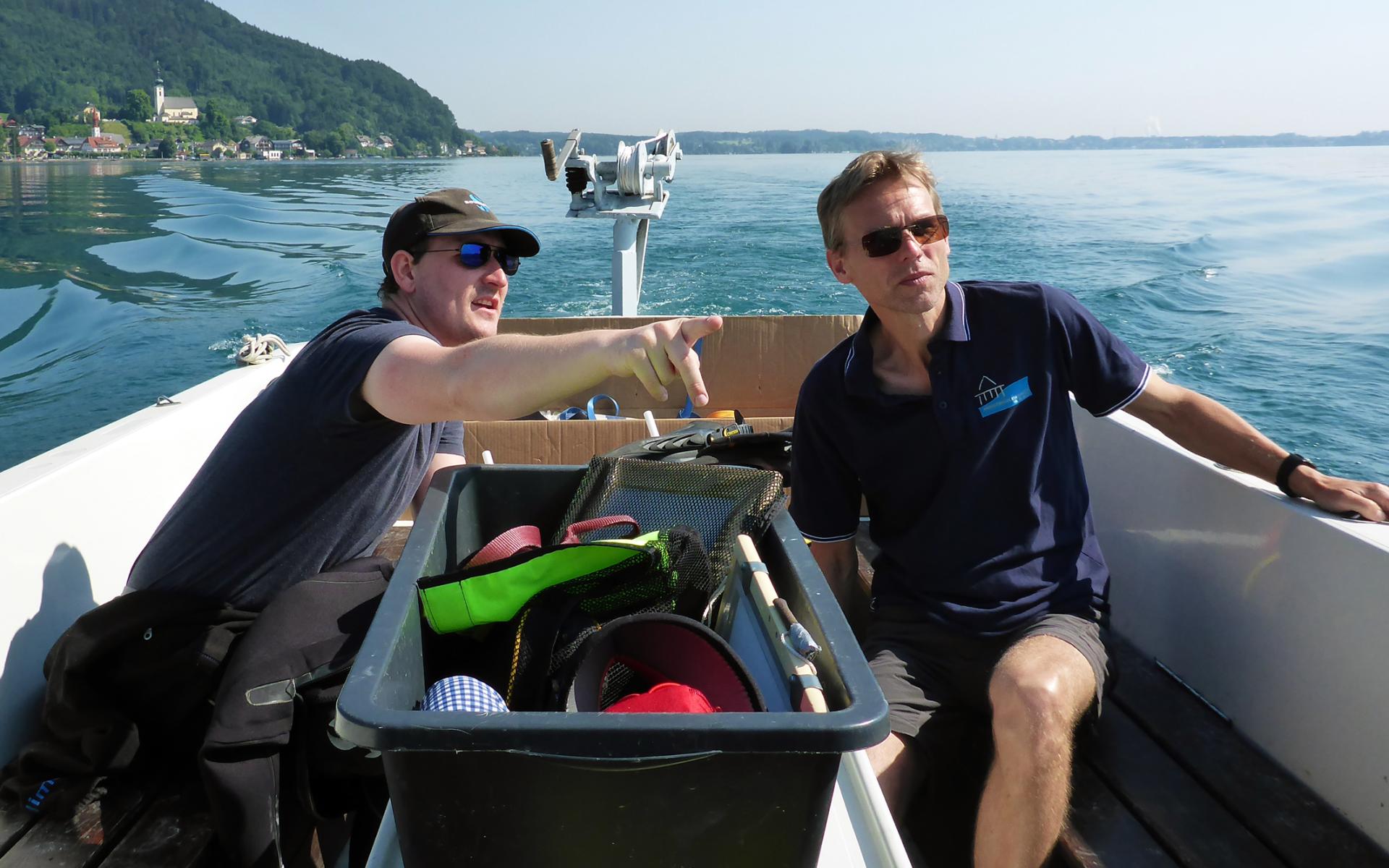 2 Männer sitzen mit Sonnenbrillen auf einem Boot am See
