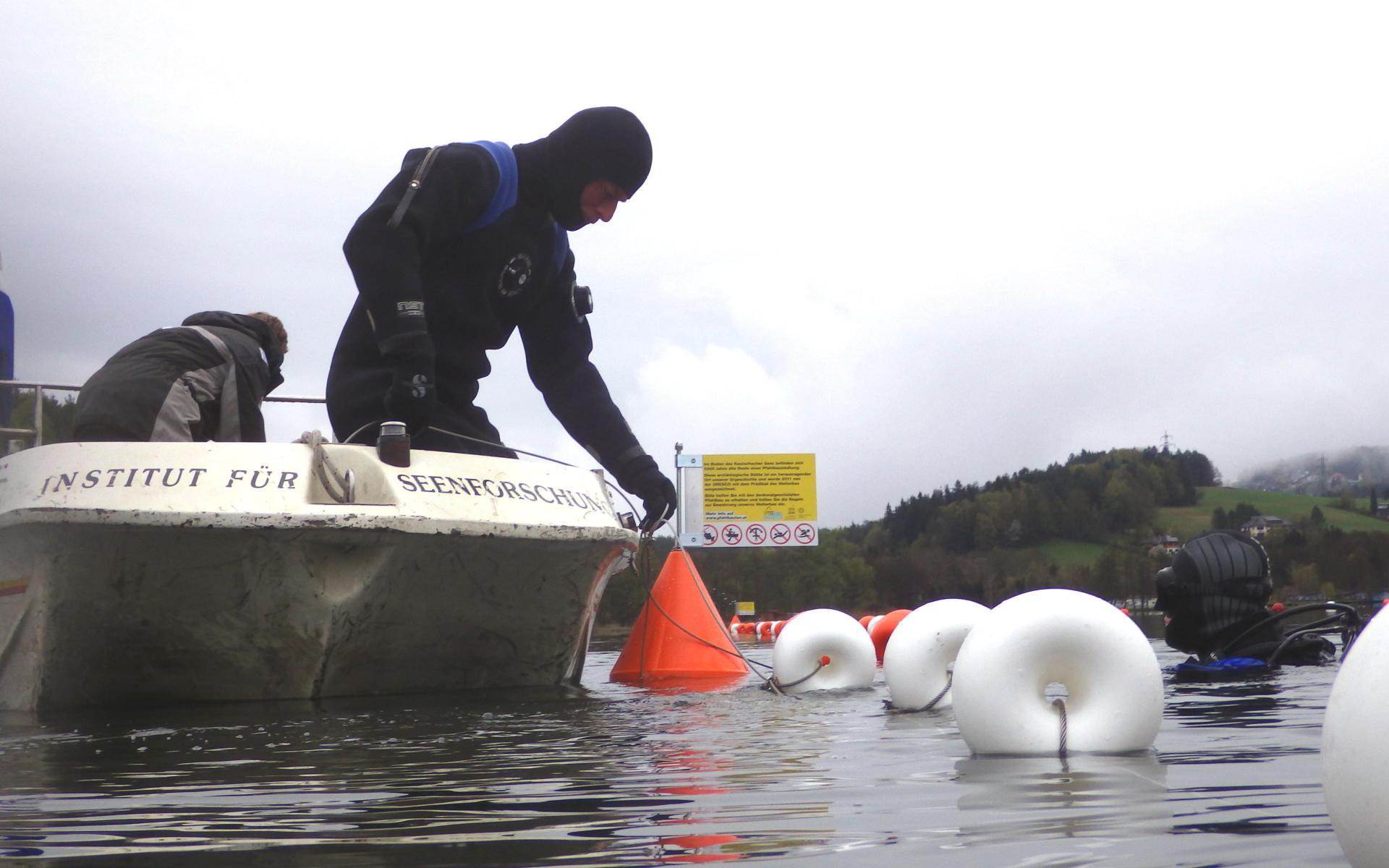 Ein Mann im Tauchanzug an Bord eines Bootes setzt Markierungsbojen in den See