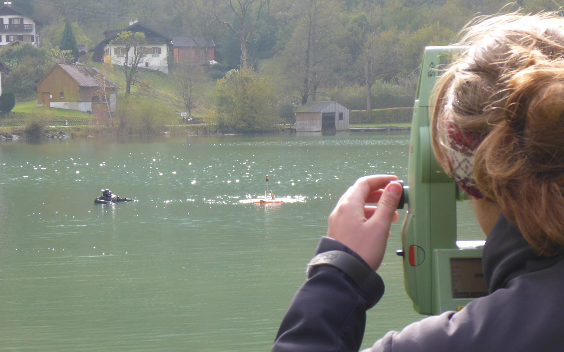 Eine Frau steht am Tachymeter und blickt auf den See, wo ein Taucher an der Oberfläche erkennbar ist