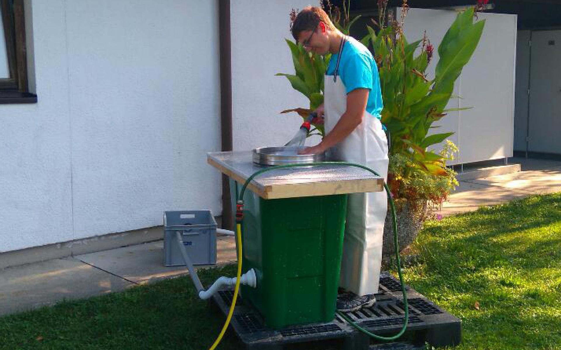 Florian mit einer Schürze, steht an der Schlämmstation und wässert das Sediment am Sieb