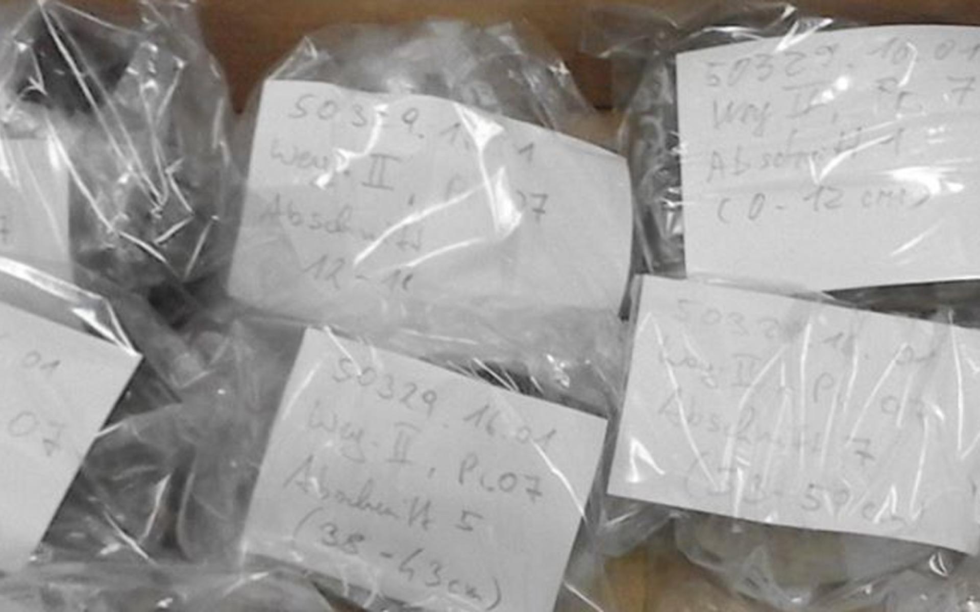 Proben in Plastikbeuteln mit handschriftlichen Beschriftungen auf weißem Papier