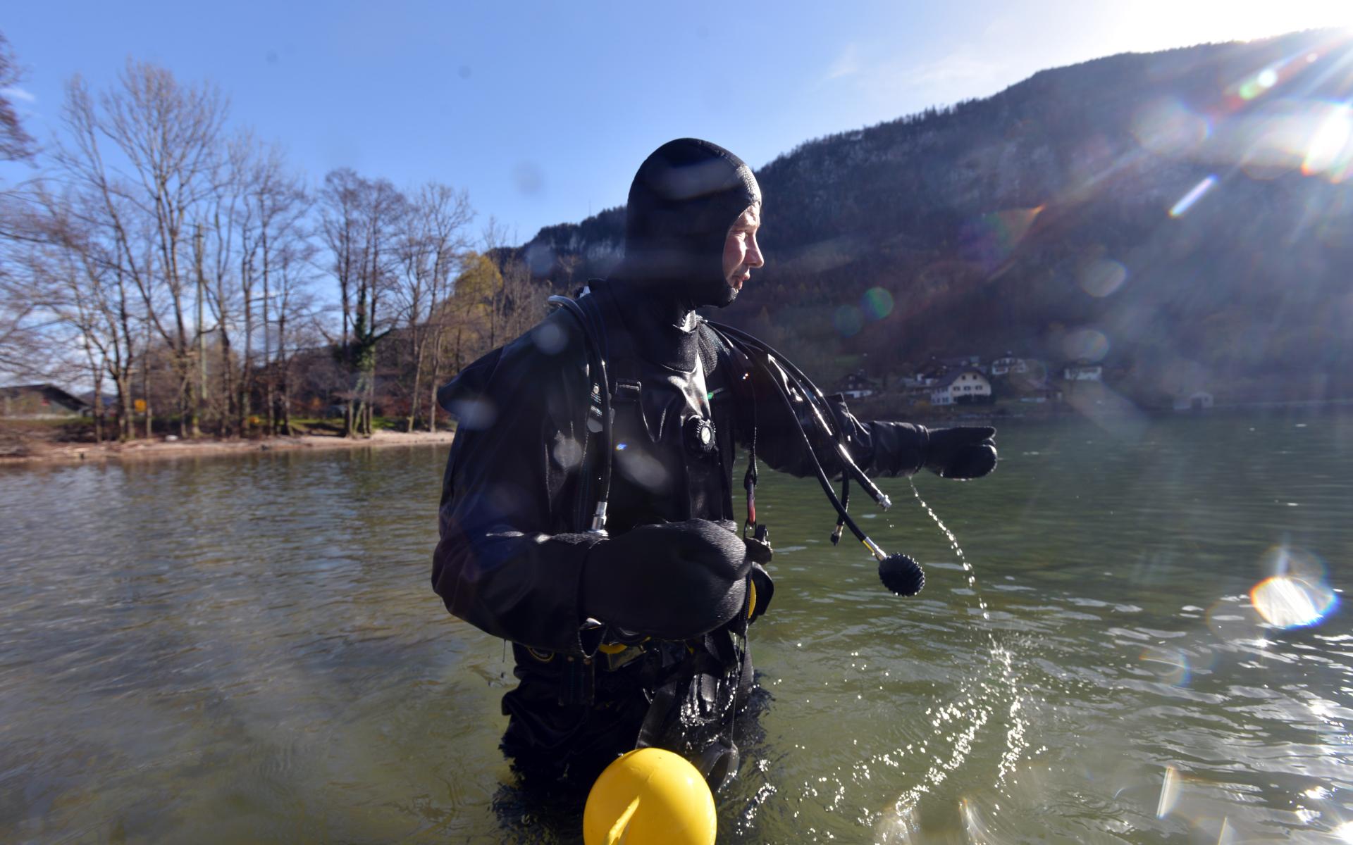 Ein Taucher steht bis zu den Hüften im Wasser und blickt auf den See