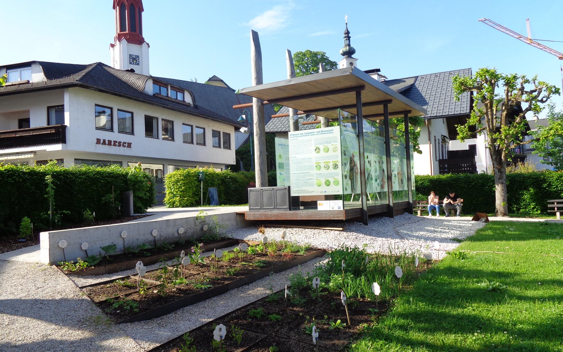 Direkt am Pfahlbaupavillon sind 2 Beete angelegt, im Hintergrund sieht man die Kirche
