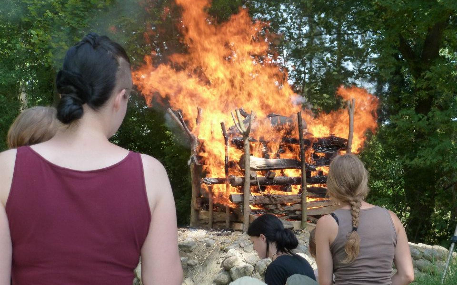 Ein Scheiterhaufen in Vollbrand wird von Student:Innen betrachtet