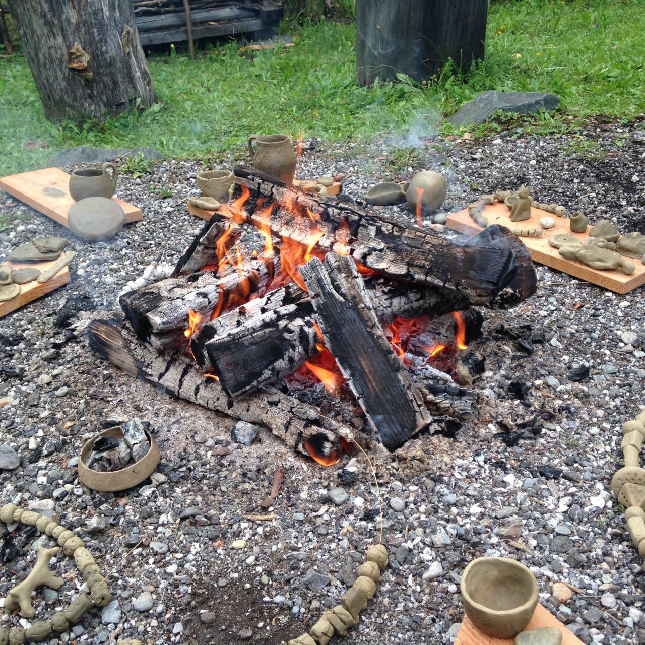 Feuchte Keramikgefäße liegen rund um brennende Holzscheite