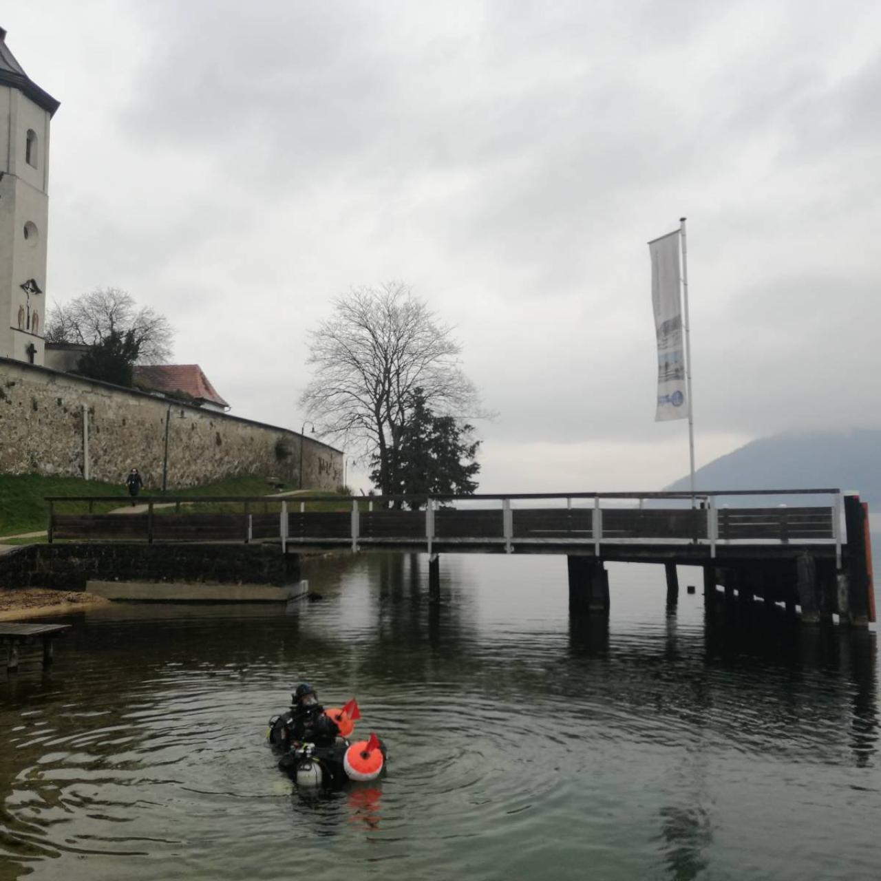 Taucher:Innen im Flachwasserbereich des Traunsees vor dem Hintergrund des Klosters Traunkirchen