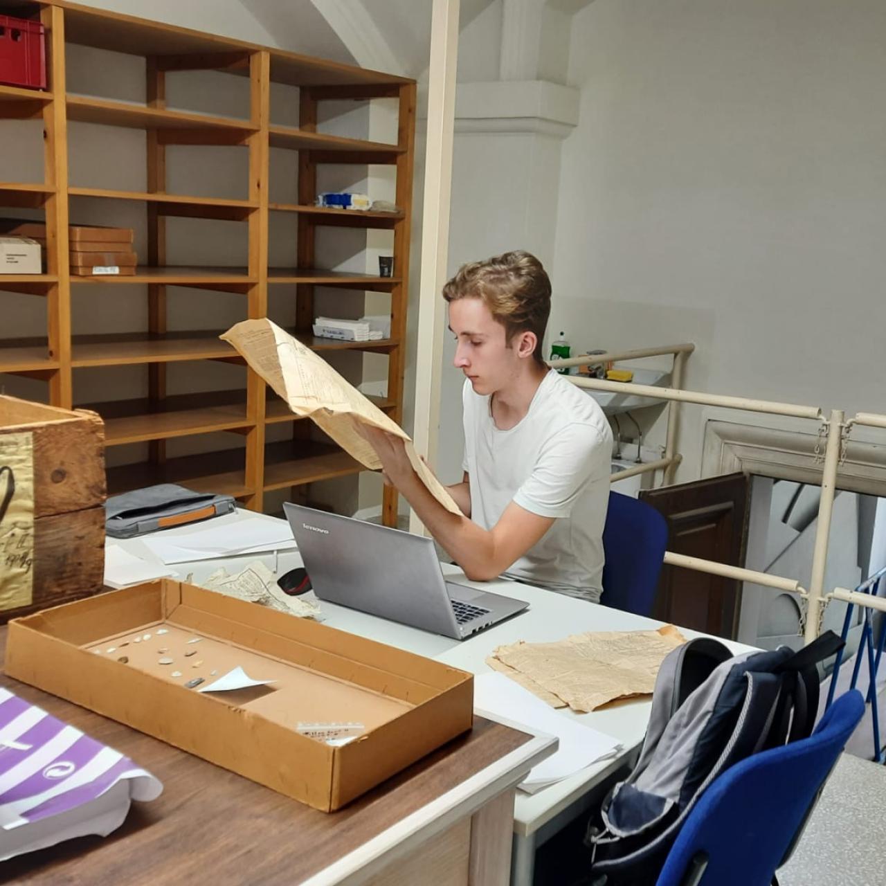 Eine Person sitzt in einem Archiv und liest eine alte Zeitung