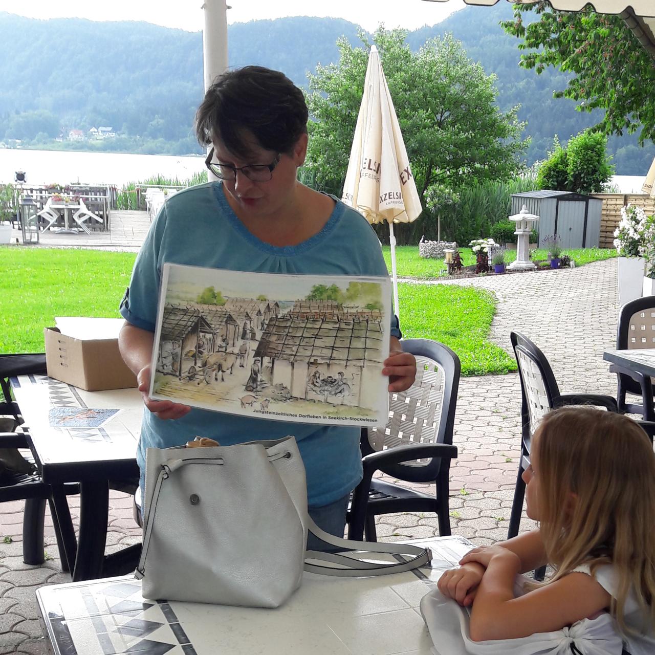 Lieselore erklärt Kindern etwas anhand einer Illustration in einem Strandcafe.