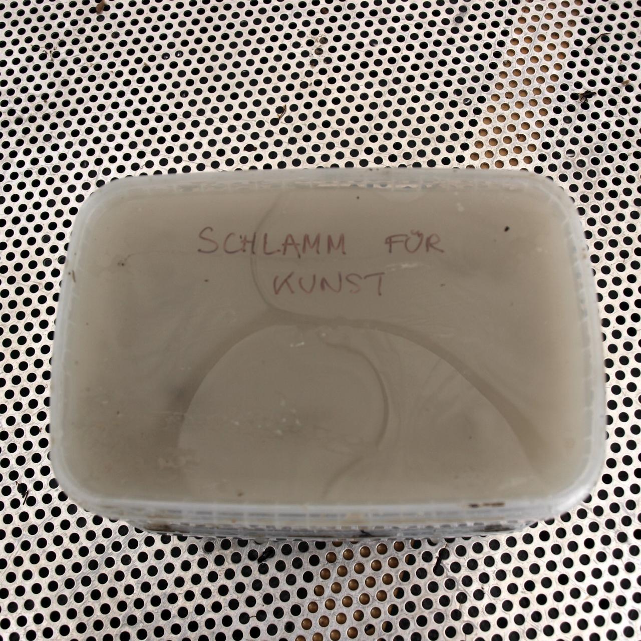 Ein Plastikbecher mit Schlamm und der Aufschrift "Schlamm für Kunst"