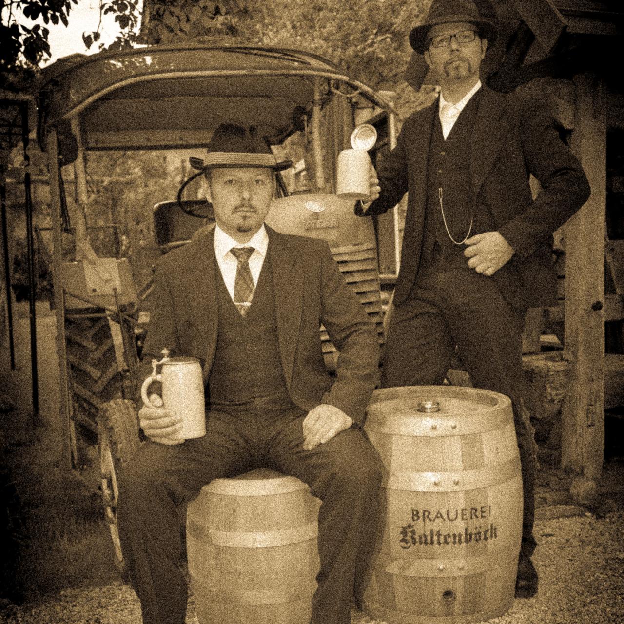 Die Brüder Kaltenböck neben Bierfässern und mit Bierkrügen in der Hand