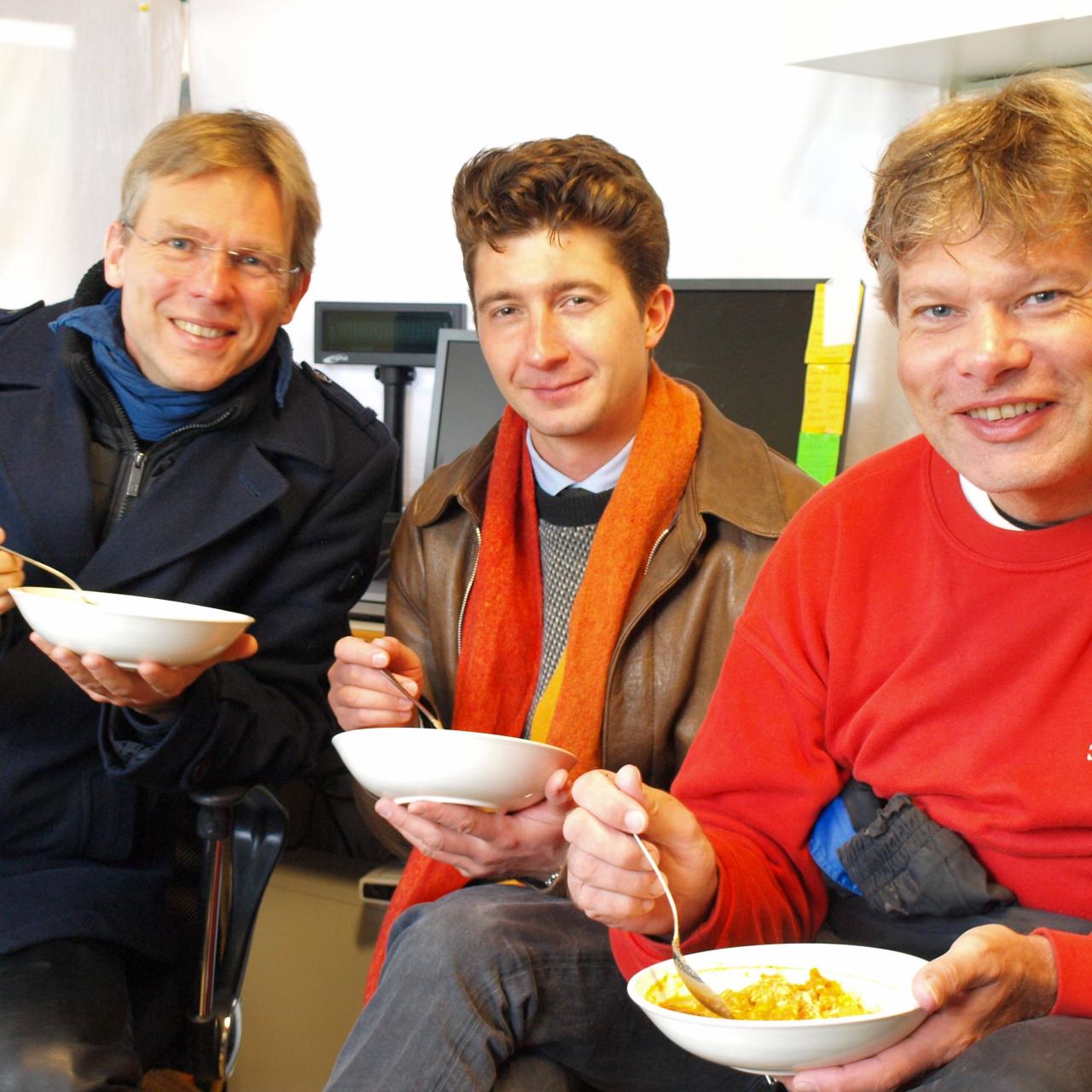 3 Personen sitzen mit Schüsselchen voll Curry im Büro
