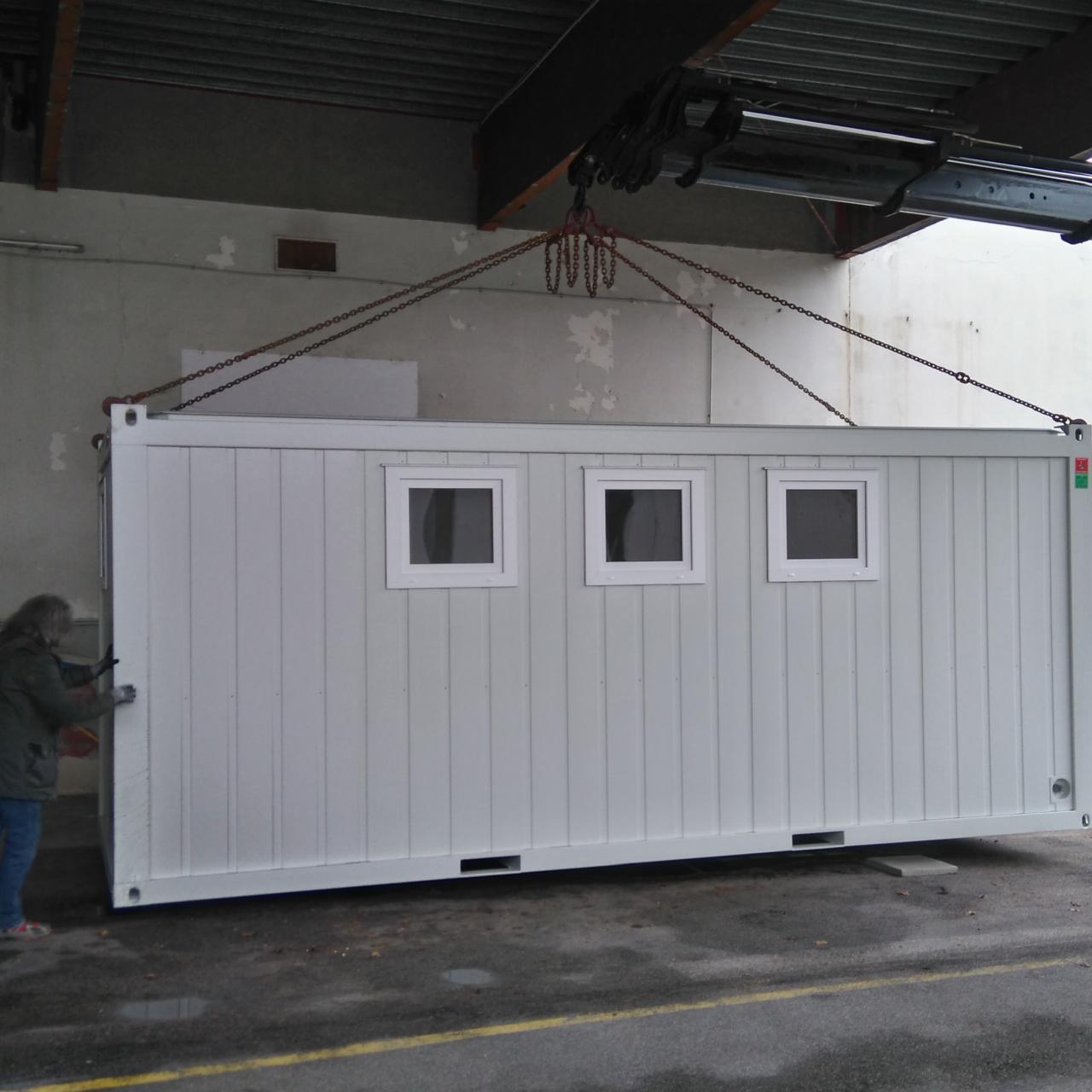 2 Arbeiter und ein Kranwagen heben den weißen Container an seinen Platz