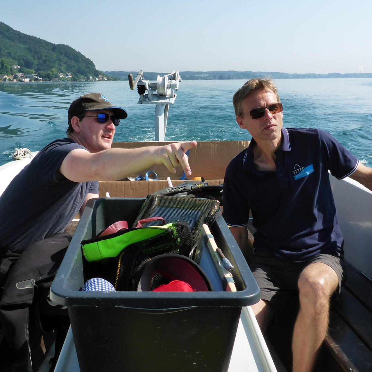 2 Männer sitzen mit Sonnenbrillen auf einem Boot am See