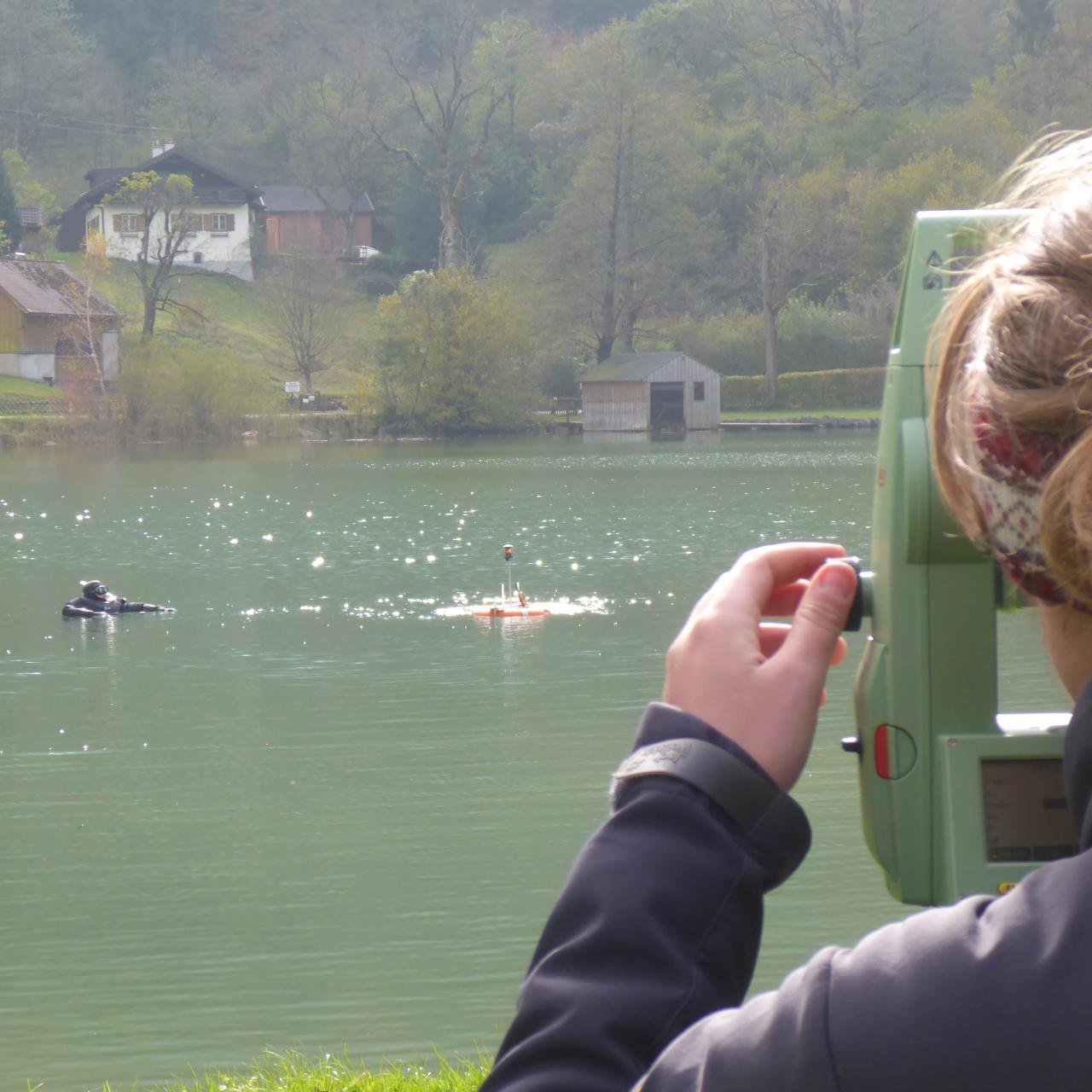 Eine Frau steht am Tachymeter und blickt auf den See, wo ein Taucher an der Oberfläche erkennbar ist