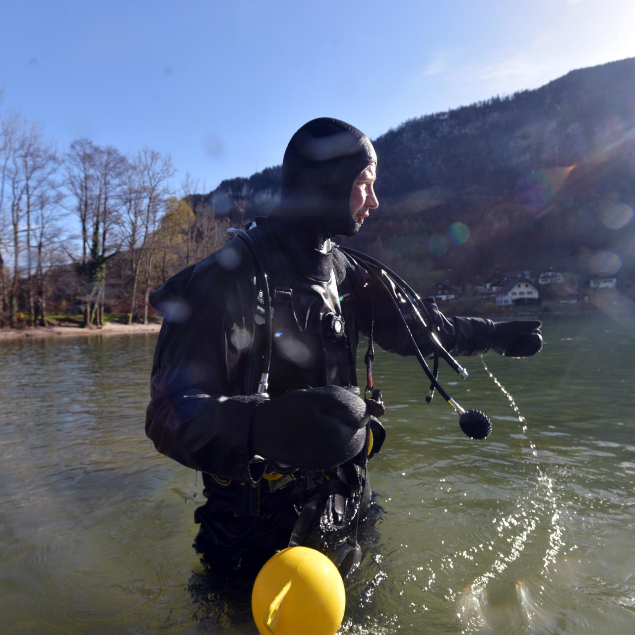 Ein Taucher steht bis zu den Hüften im Wasser und blickt auf den See