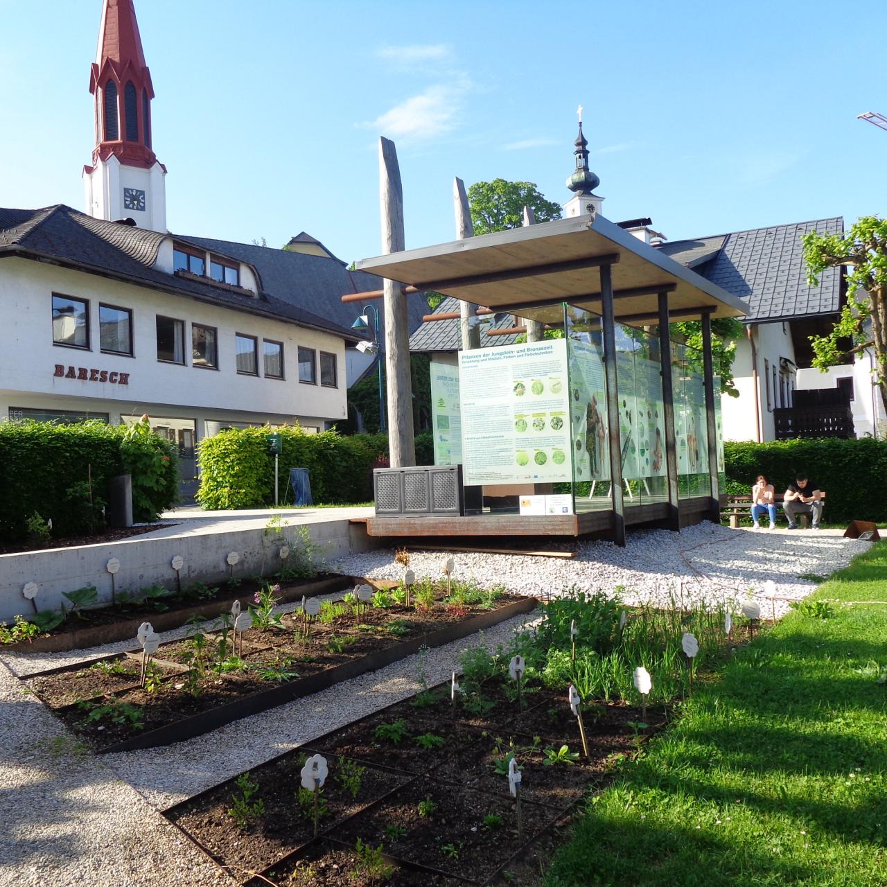Direkt am Pfahlbaupavillon sind 2 Beete angelegt, im Hintergrund sieht man die Kirche