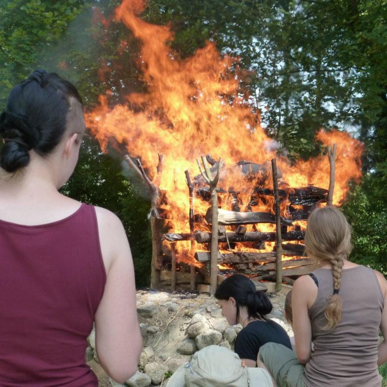 Ein Scheiterhaufen in Vollbrand wird von Student:Innen betrachtet